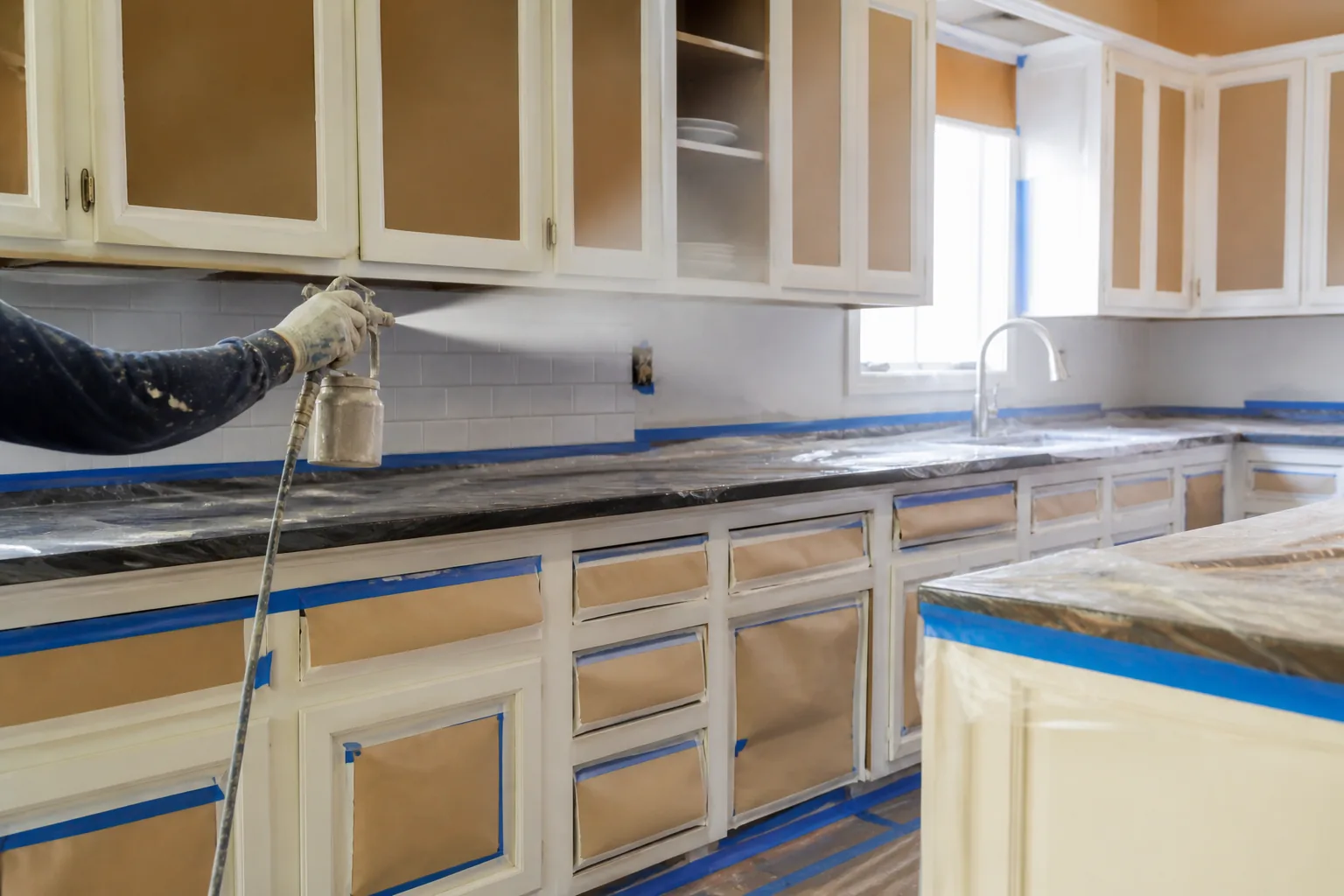 Painter spraying primer on kitchen cabinet doors and drawer fronts with the countertops masked off: Painted, painted cabinets, doors