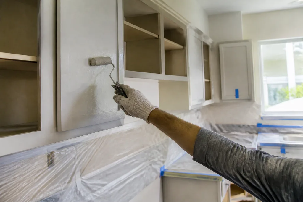 Painter rolling primer onto an upper kitchen cabinet door with the counters covered in plastic: Painted, painted cabinets, doors